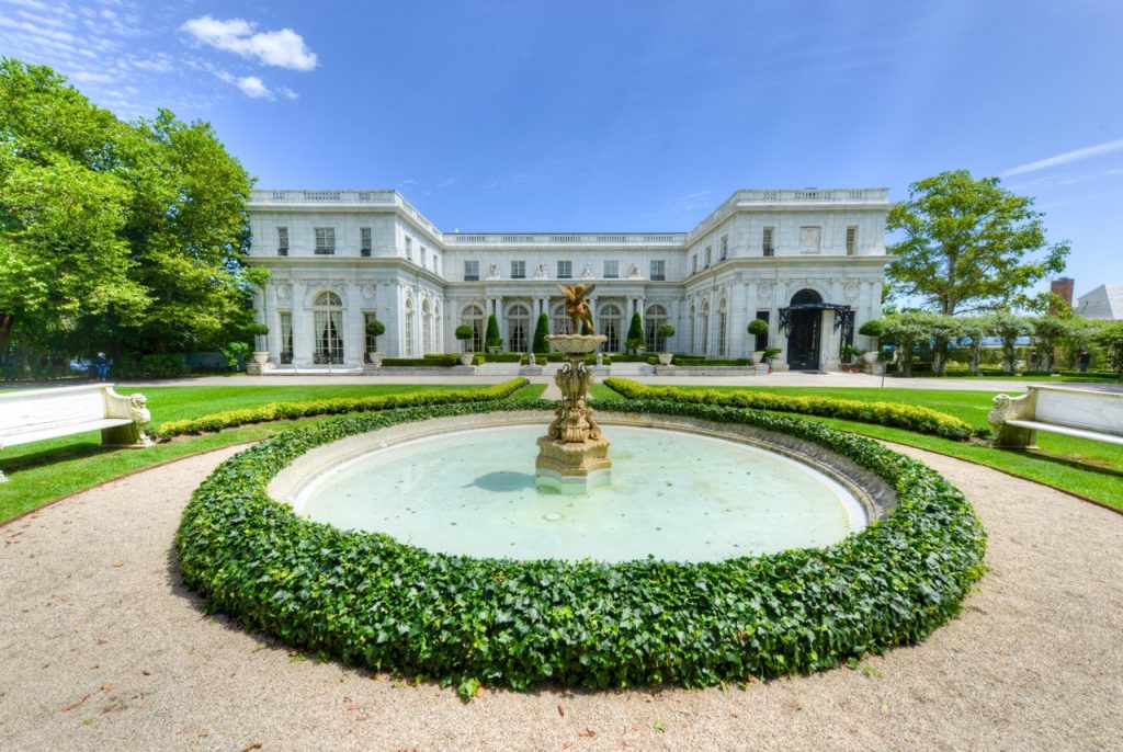 Luxury estate home featuring a circular driveway landscape with a manicured hedge and a central stone fountain.