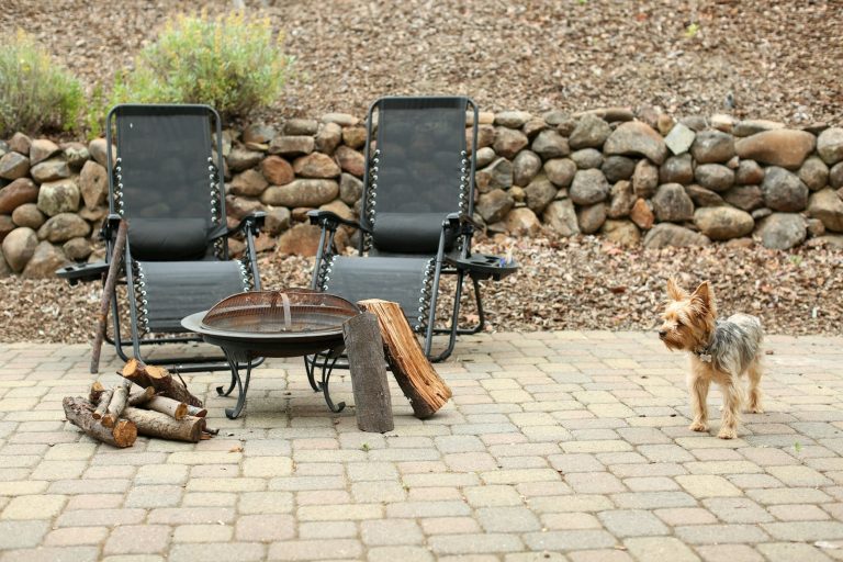 Brick paver patio with two lounge chairs around a fire pit, the kind of Birmingham MI outdoor living space that needs sealing and joint sand before winter